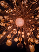 An intricate overhead arrangement of lanterns with warm, glowing lights. The lanterns are suspended from wooden beams, creating a symmetrical and visually captivating pattern. The background is dark, accentuating the warm hues of the lanterns.