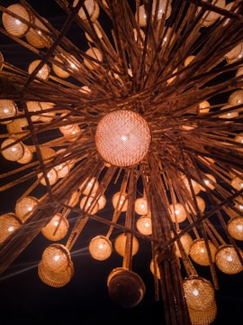 An intricate overhead arrangement of lanterns with warm, glowing lights. The lanterns are suspended from wooden beams, creating a symmetrical and visually captivating pattern. The background is dark, accentuating the warm hues of the lanterns.