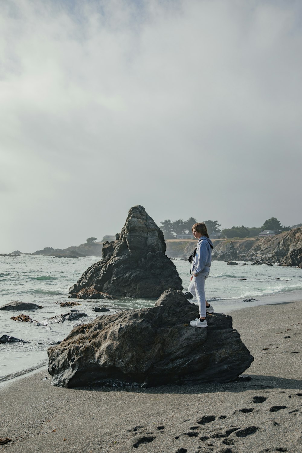 a woman standing on top of a rock near the ocean