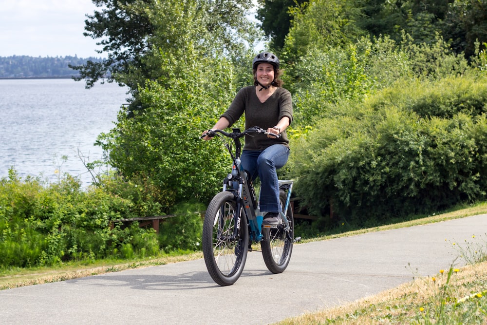 a woman riding a bike down a path next to a lake