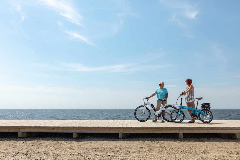 a man and a woman standing on a pier with their bikes