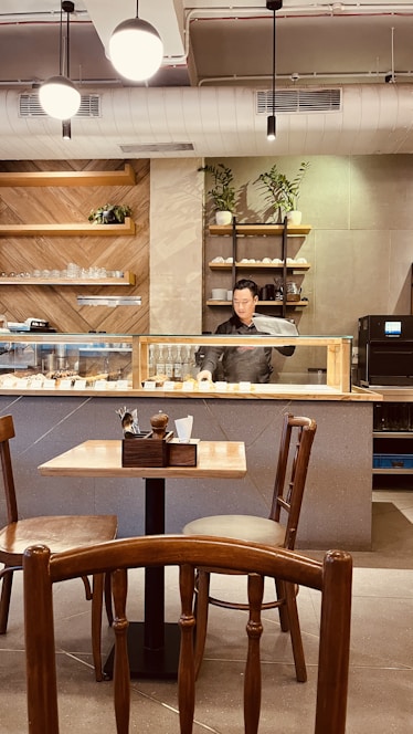 A warm, inviting cafe interior with wooden tables, soft lighting, and a barista preparing coffee behind the counter.
