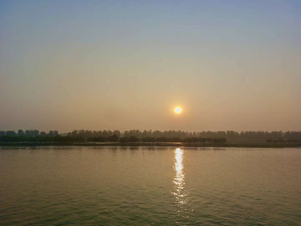 Sunset over water with trees on horizon, reflecting warm orange-yellow sky colors