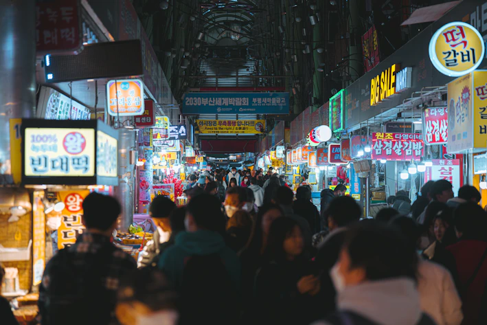 A vibrant street market scene showing various food stalls with colorful signage and happy customers.