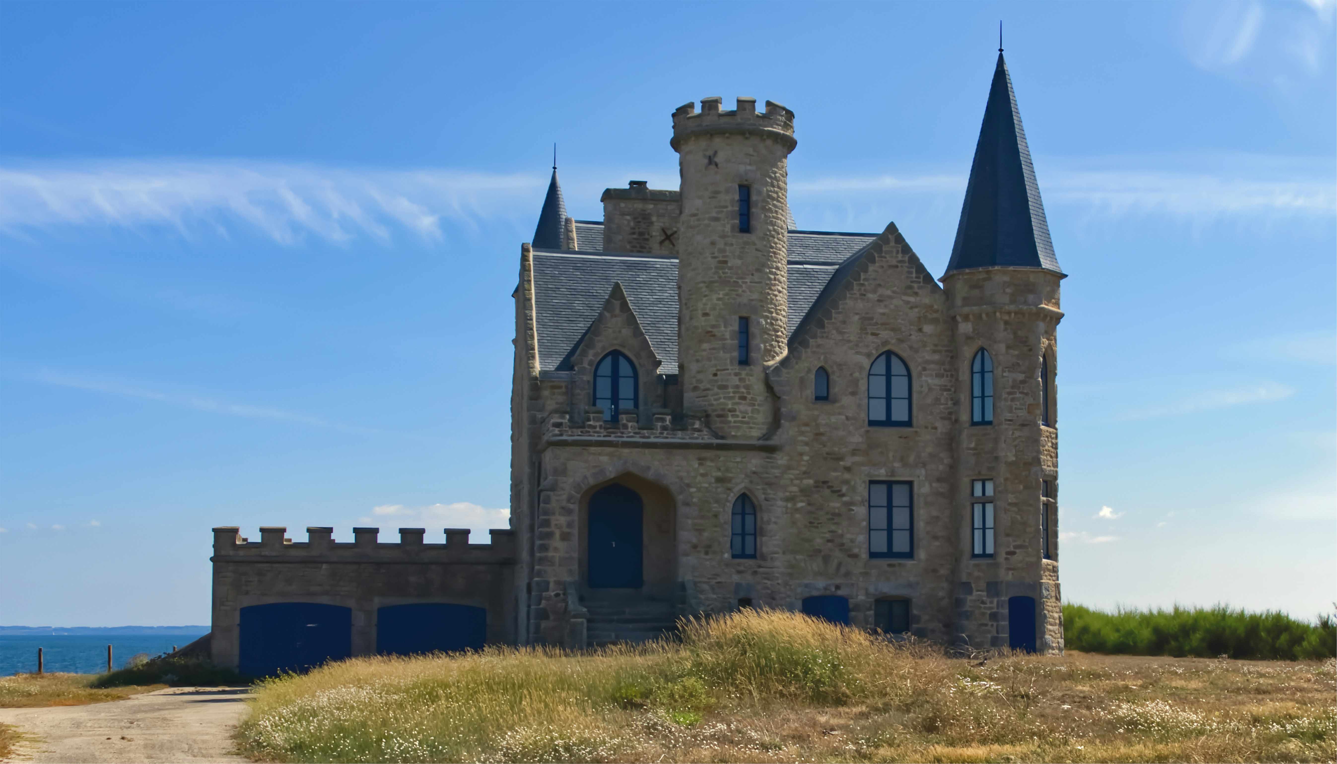 a castle like building with a blue door and two towers, Le Château Turpault Au début du xxe siècle, Georges Turpault, un filateur de Cholet, achète une vieille demeure et le terrain attenant sur la pointe de Beg-er-Lann, située au sud-ouest de la côte Sauvage de la presqu