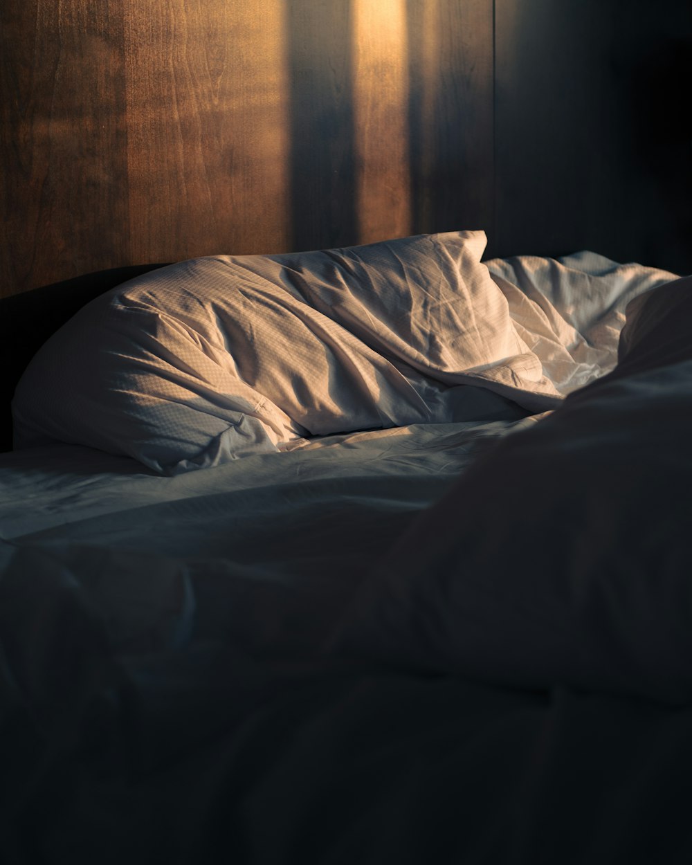 an unmade bed with a wooden head board