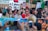 A large group of people participating in a protest or demonstration, holding colorful banners and signs with environmental messages. Some individuals have painted faces and are wearing traditional or cultural attire.