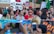 A large group of people participating in a protest or demonstration, holding colorful banners and signs with environmental messages. Some individuals have painted faces and are wearing traditional or cultural attire.