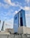 A series of modern skyscrapers stand under a blue sky with scattered clouds. The tall glass buildings reflect the sky, with the largest building prominently displaying 'LANDMARK GROUP' on its facade. Surrounding structures vary in height and design, adding to the urban cityscape.
