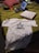 A casual setting featuring a bed with a laptop, a white T-shirt with the text 'WE SHOULD ALL BE FEMINISTS', a pizza box, and a game controller. The bed has a green cover and pillows, creating a cozy atmosphere.