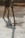 A construction worker is pouring wet concrete over a grid of rebar on a construction site. The worker is wearing boots and is holding a large hose that dispenses the concrete onto the surface. Shadows are cast on the textured surface as the concrete spreads out.
