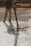 A construction worker is pouring wet concrete over a grid of rebar on a construction site. The worker is wearing boots and is holding a large hose that dispenses the concrete onto the surface. Shadows are cast on the textured surface as the concrete spreads out.