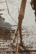 Concrete is being poured onto a construction site through a large hose. Rebar is visible, indicating reinforcement work for a foundation or slab. The surrounding area appears organized, with construction tools partially visible.