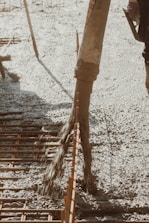 Concrete is being poured onto a construction site through a large hose. Rebar is visible, indicating reinforcement work for a foundation or slab. The surrounding area appears organized, with construction tools partially visible.