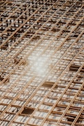 Reinforced steel bars arranged in a grid pattern on a construction site, with a bright sunlight reflection causing a lens flare effect.