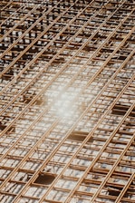 Reinforced steel bars arranged in a grid pattern on a construction site, with a bright sunlight reflection causing a lens flare effect.