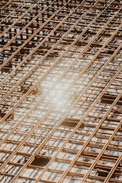 Reinforced steel bars arranged in a grid pattern on a construction site, with a bright sunlight reflection causing a lens flare effect.