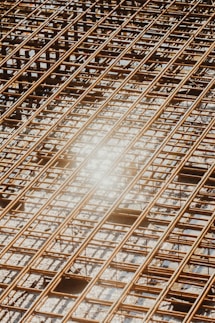 Reinforced steel bars arranged in a grid pattern on a construction site, with a bright sunlight reflection causing a lens flare effect.