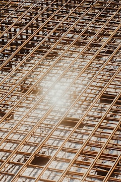 Reinforced steel bars arranged in a grid pattern on a construction site, with a bright sunlight reflection causing a lens flare effect.