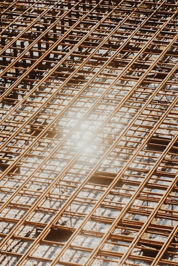 Reinforced steel bars arranged in a grid pattern on a construction site, with a bright sunlight reflection causing a lens flare effect.