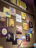 A wall display features various album covers and posters related to The Beatles and their individual members. The arrangement is colorful and artistic, showcasing different portraits and designs. A prominent sign at the top reads 'THE BEATLES Discography,' highlighting the theme of the collection.
