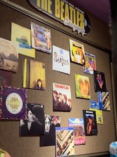 A wall display features various album covers and posters related to The Beatles and their individual members. The arrangement is colorful and artistic, showcasing different portraits and designs. A prominent sign at the top reads 'THE BEATLES Discography,' highlighting the theme of the collection.
