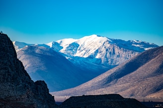 A stunning panoramic shot of snow-capped mountains under a clear blue sky at sunrise.