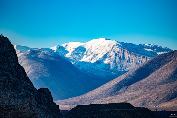 A stunning panoramic shot of snow-capped mountains under a clear blue sky at sunrise.