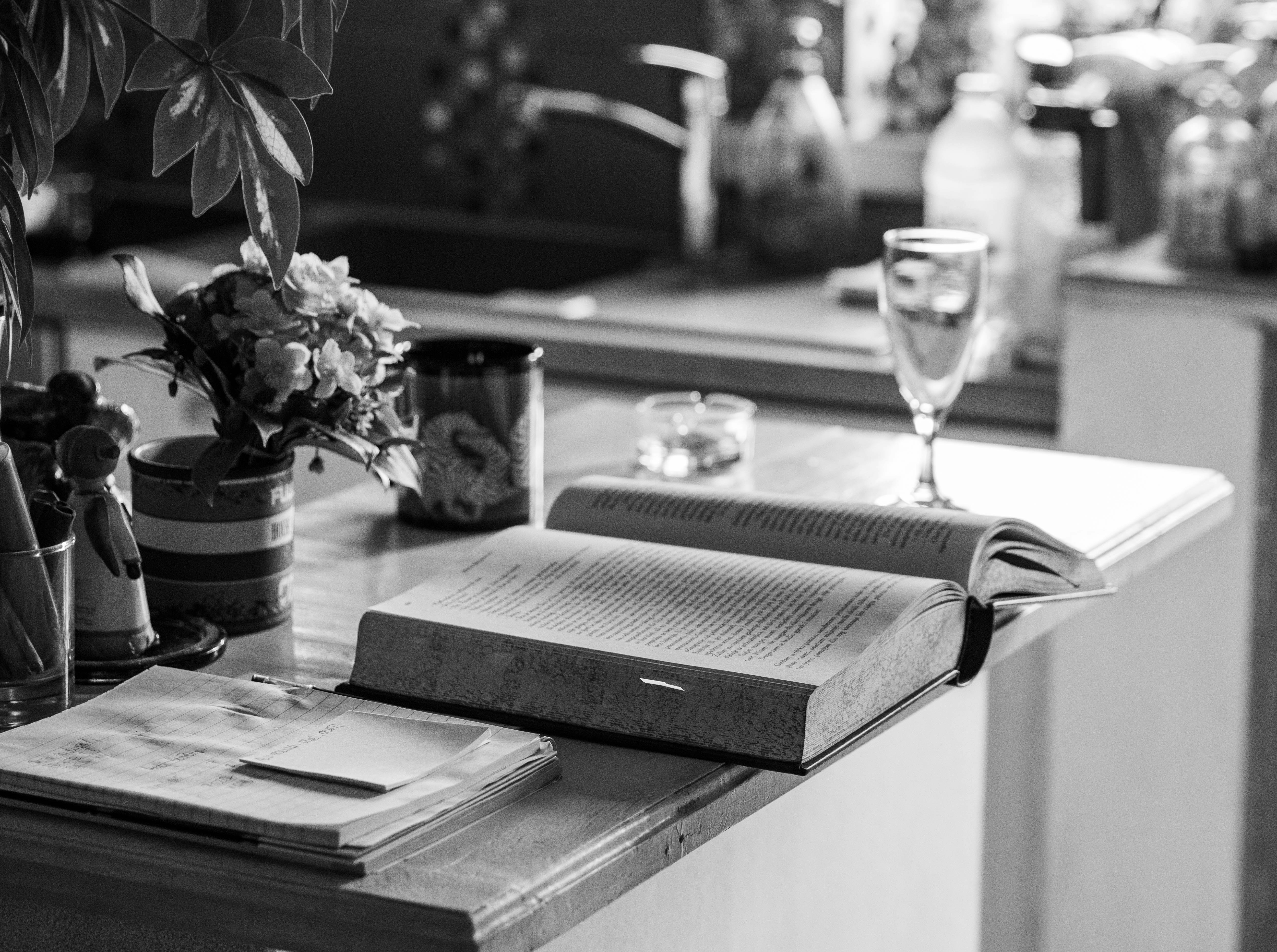 an open book sitting on top of a counter next to a vase of flowers