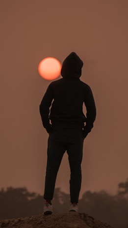 An outdoor scene with a person wearing an Orion Alpha Outfitters hoodie, standing against a sunset backdrop.