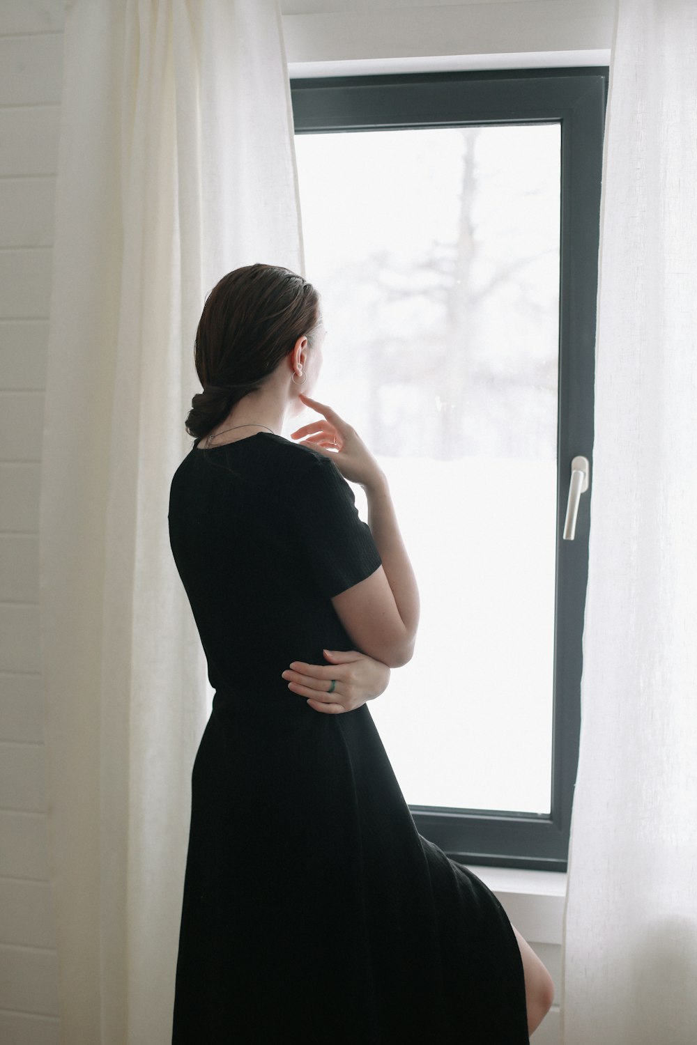 a woman in a black dress looking out a window