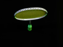 A professional badminton player gripping a sleek Sparta racket mid-swing in a bright indoor court.