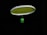 A badminton racket is suspended in the air against a black background. The strings of the racket are illuminated in a bright lime green color, contrasting with the dark surroundings. The handle of the racket is partially visible in a blurred focus.