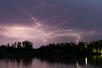 A vivid lightning strike captured over a calm lake reflecting the stormy sky.