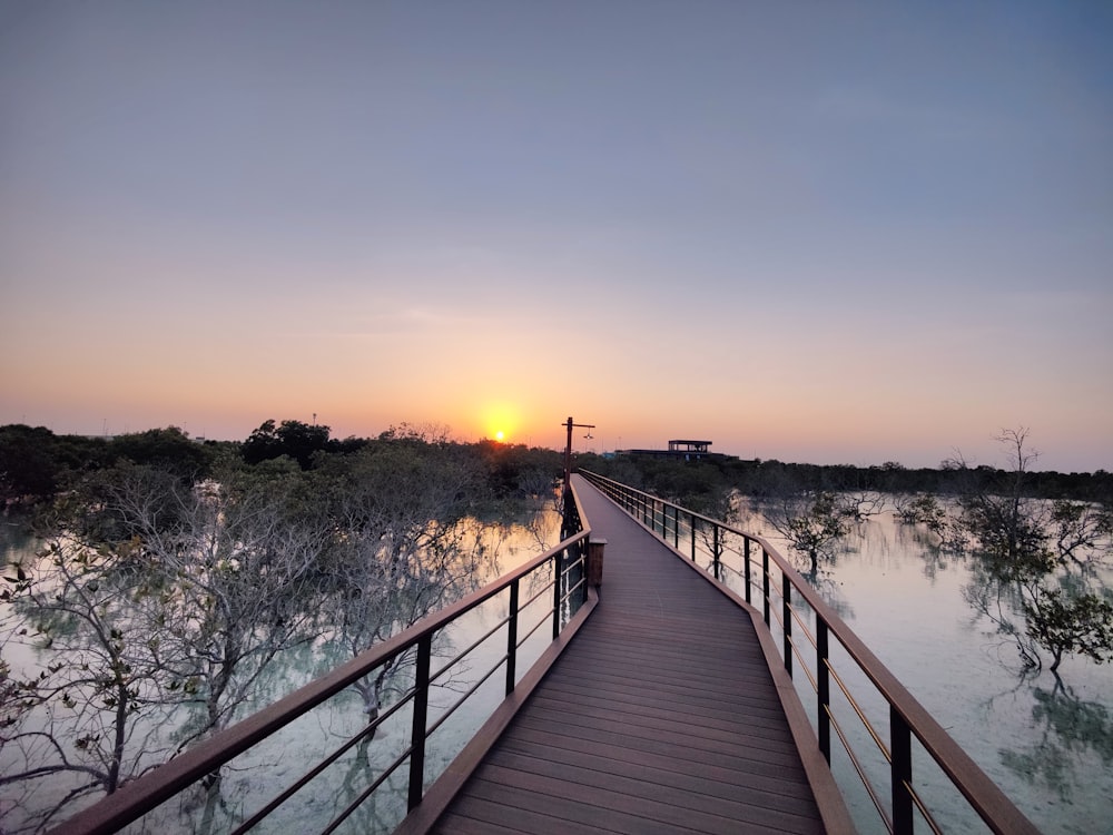 a wooden walkway leading to a lake at sunset