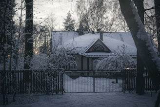 a house covered in snow next to a fence