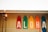 Five colorful surfboards are displayed vertically against a wall with the letters spelling 'ALOHA'. Two tiki torches are lit in the foreground, adding a warm, tropical vibe. Multicolored string lights are hung along the roofline above the surfboards.