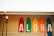 Five colorful surfboards are displayed vertically against a wall with the letters spelling 'ALOHA'. Two tiki torches are lit in the foreground, adding a warm, tropical vibe. Multicolored string lights are hung along the roofline above the surfboards.