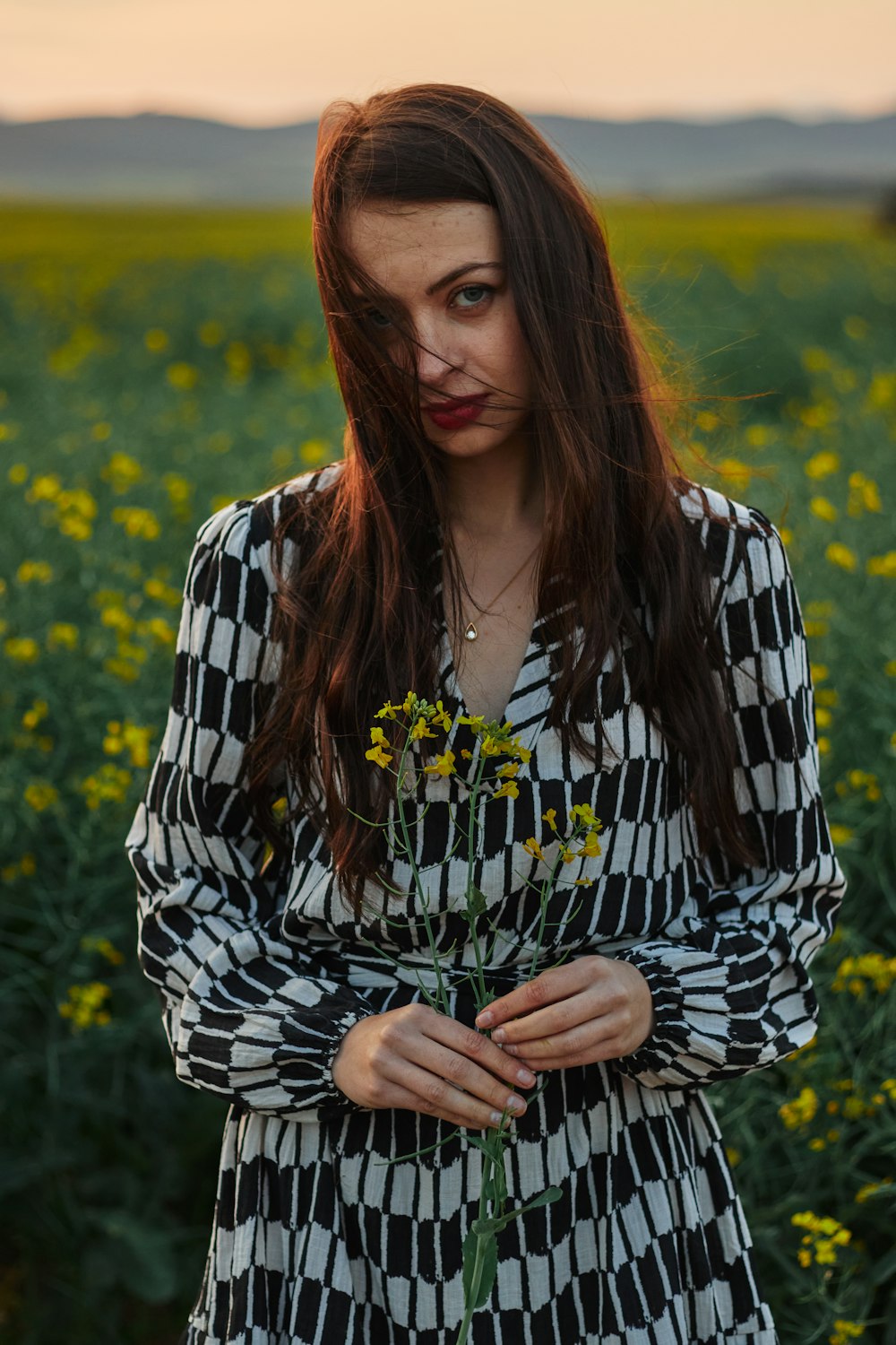 a woman standing in a field holding a flower