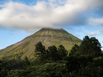 a very tall mountain surrounded by trees under a cloudy sky