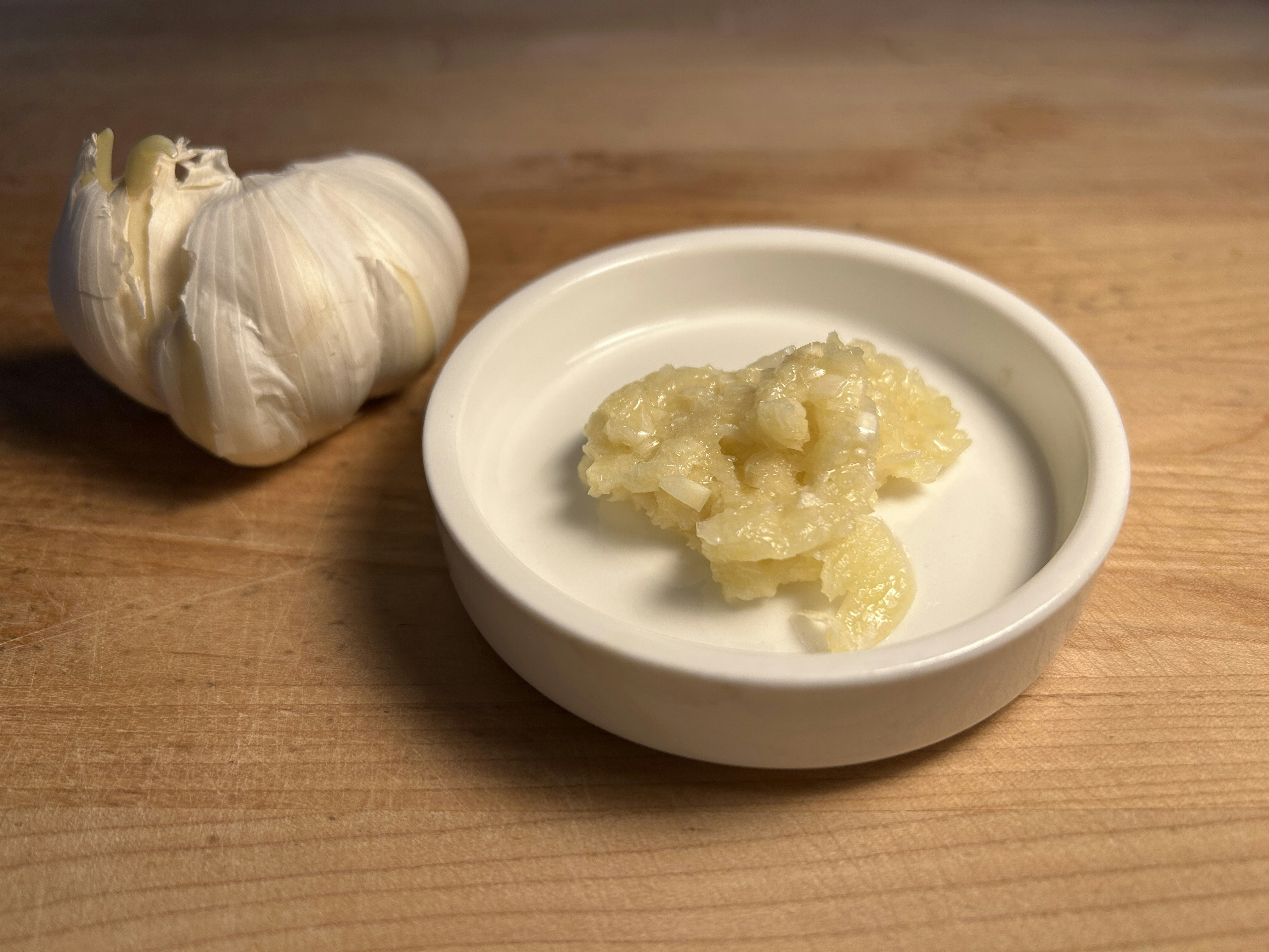 Creamy white garlic paste in a small glass jar with whole garlic cloves on a light wooden surface