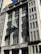 A grand building showcasing a classic architectural style, characterized by its symmetrical facade and large windows. The focal point is an ornate clock mounted on the exterior, surrounded by intricate detailing. The building displays the name 'The Guardian' above the entrance.