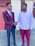 Two men are shaking hands outdoors, both dressed in formal attire. The man on the left is wearing a maroon blazer with a white shirt and a maroon tie, while the man on the right is in a white shirt and maroon trousers. They appear to be engaged in a friendly and positive interaction.