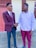 Two men are shaking hands outdoors, both dressed in formal attire. The man on the left is wearing a maroon blazer with a white shirt and a maroon tie, while the man on the right is in a white shirt and maroon trousers. They appear to be engaged in a friendly and positive interaction.
