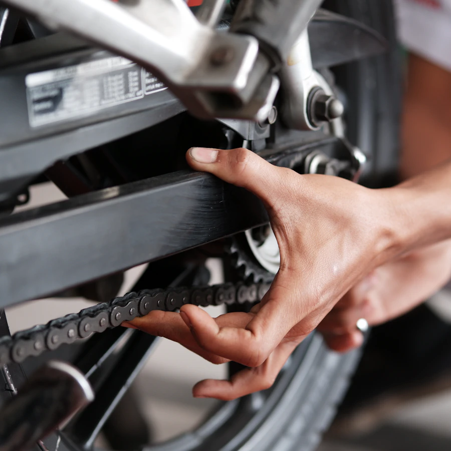 Hands adjusting a motorcycle drive chain at the swingarm and rear sprocket