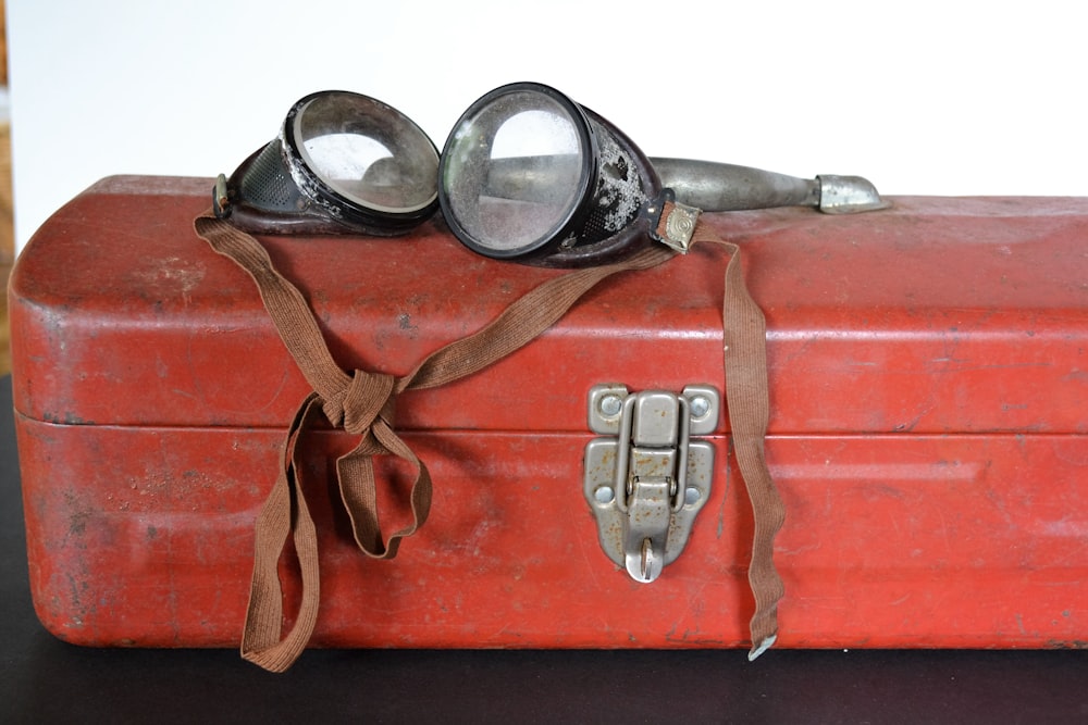 a pair of goggles sitting on top of a red suitcase