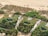 Aerial view of several small buildings with green roofs, surrounded by lush vegetation. The structures appear to be nestled close to a sandy beach, with a backdrop of natural shrubbery and expanses of sand.