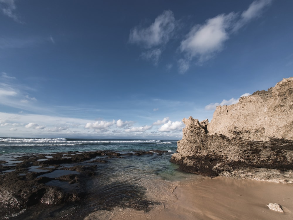 a sandy beach with rocks and water under a blue sky