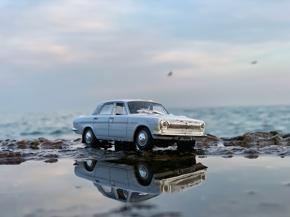 a toy car sitting on top of a beach next to the ocean