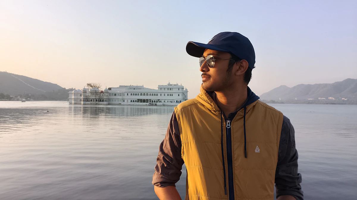 A man standing on a boat with the lake behind him in warm light